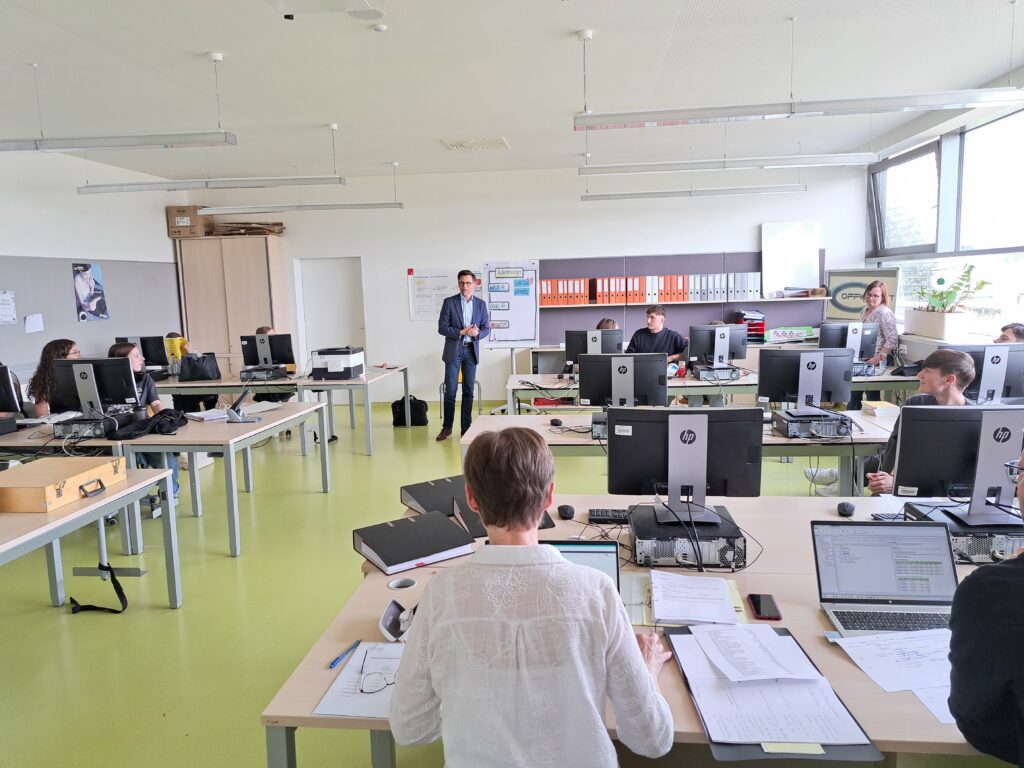 Ein Raum mit mehreren Computern, in dem eine Schulung stattfindet, mit Teilnehmern und einem Referenten.