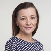 Frau mit braunen Haaren und gepunktetem Oberteil, lächelnd in die Kamera blickend.